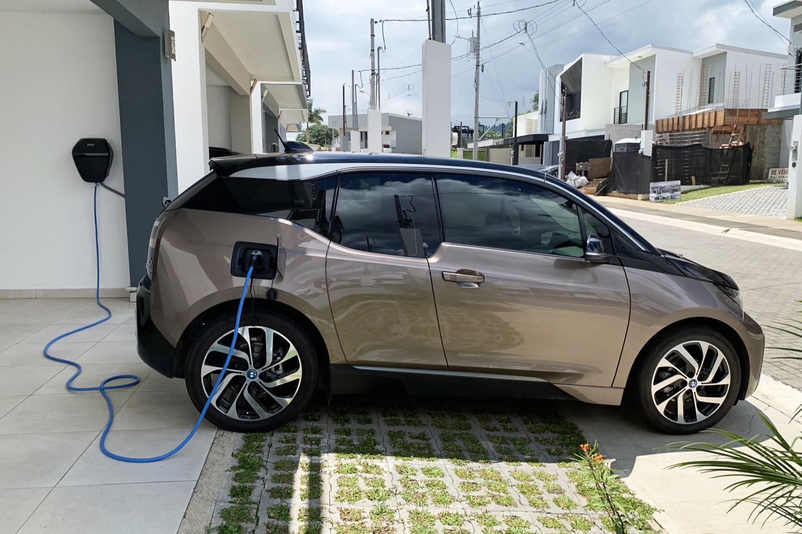 Carro eléctrico BMW i3 cargando en un wallbox residencial instalado en la pared de una vivienda